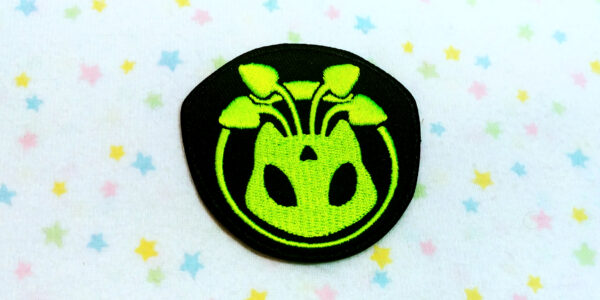 Y2K inspired Alien Aisha embroidered patch design featuring florescent green thread on a black badge shape back.
